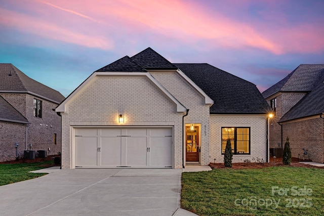 view of front of house featuring a yard, brick siding, central air condition unit, driveway, and an attached garage