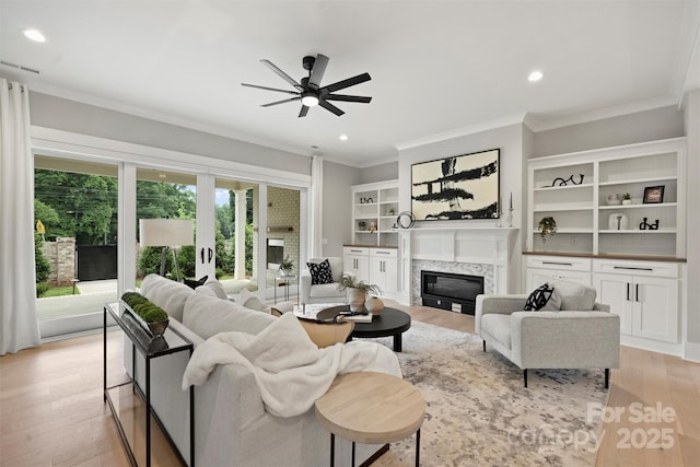 living room with light wood-type flooring, ceiling fan, crown molding, and a glass covered fireplace