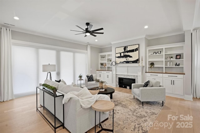 living room featuring recessed lighting, ornamental molding, a ceiling fan, and a glass covered fireplace