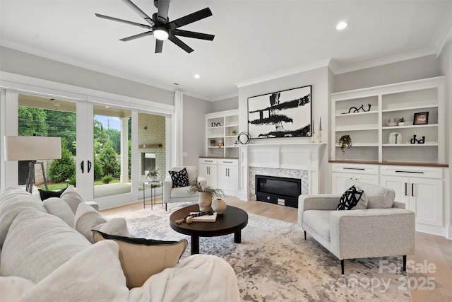 living area with ornamental molding, a ceiling fan, light wood finished floors, and a glass covered fireplace
