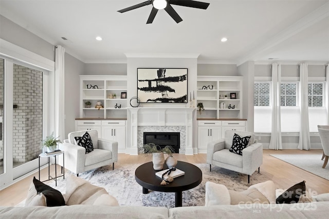living room with a premium fireplace, crown molding, a ceiling fan, and light wood-style floors
