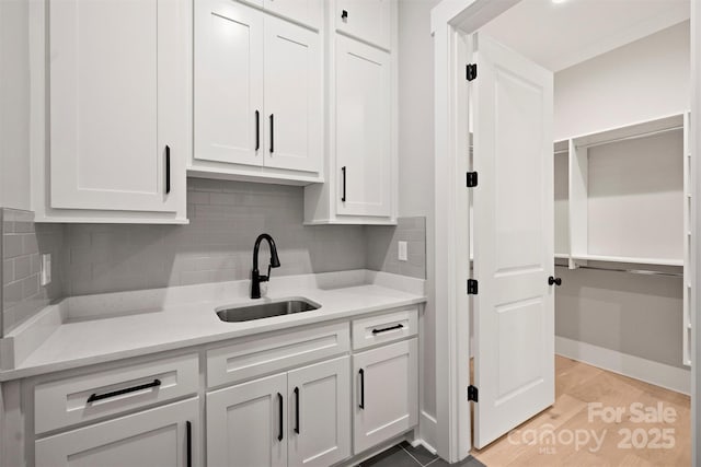 kitchen with decorative backsplash, white cabinetry, light countertops, and a sink