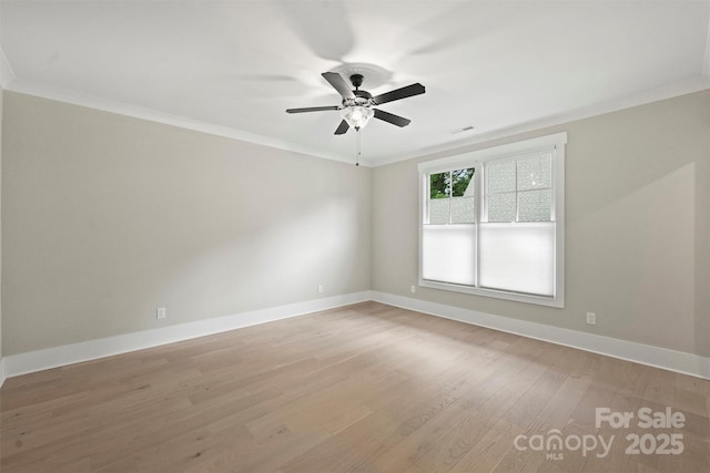 spare room featuring light wood-style floors, ceiling fan, baseboards, visible vents, and crown molding