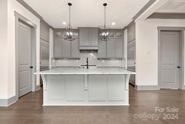 kitchen with light stone countertops, pendant lighting, an island with sink, and dark hardwood / wood-style flooring