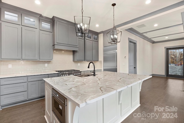 kitchen featuring dark wood-type flooring, a kitchen island with sink, light stone counters, crown molding, and built in appliances