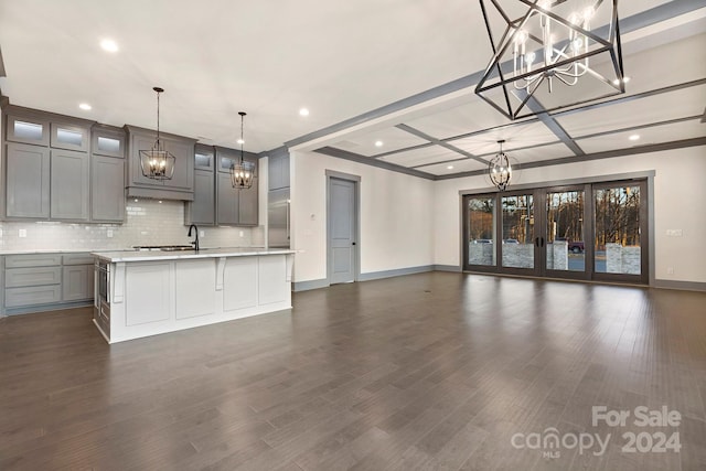 kitchen featuring gray cabinetry, backsplash, dark wood-type flooring, a center island with sink, and pendant lighting