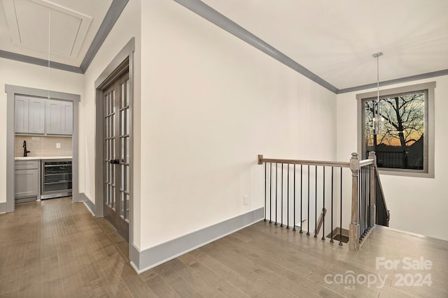 hall with crown molding, light hardwood / wood-style flooring, sink, and beverage cooler