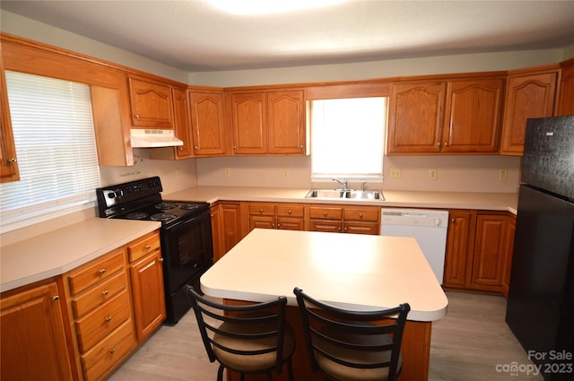 kitchen with a breakfast bar area, a kitchen island, light hardwood / wood-style flooring, black appliances, and sink