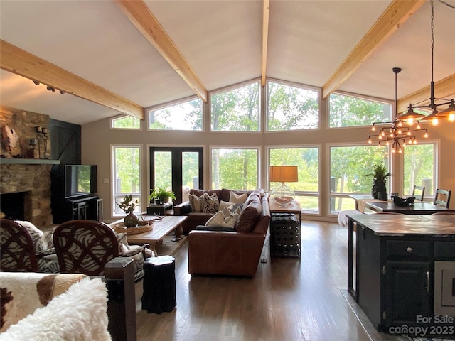 living room featuring dark wood-type flooring, a wealth of natural light, a chandelier, and a stone fireplace