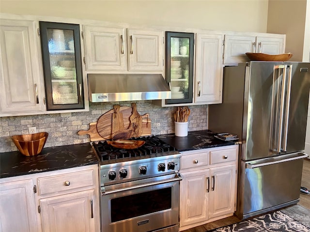 kitchen with tasteful backsplash, hardwood / wood-style flooring, white cabinetry, high end appliances, and wall chimney range hood