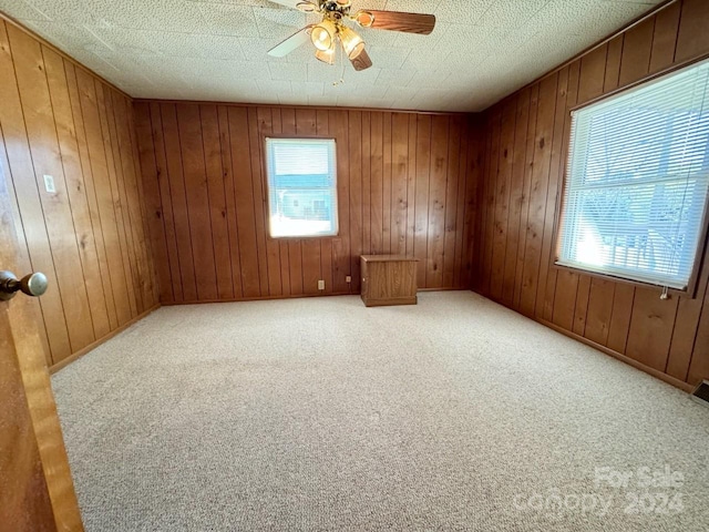 unfurnished room with carpet floors, ceiling fan, wood walls, and a textured ceiling