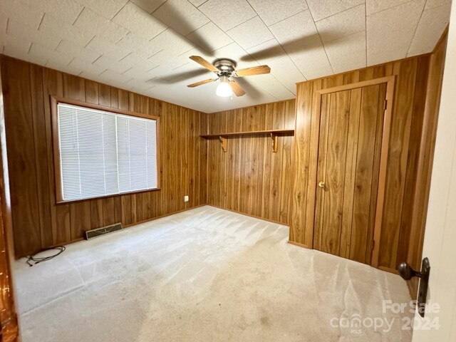 spare room with ceiling fan, wood walls, and carpet