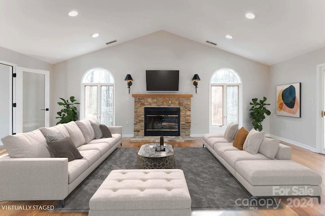 living room with wood-type flooring, a stone fireplace, and vaulted ceiling