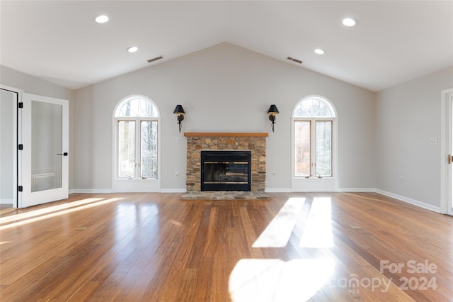 unfurnished living room with a stone fireplace, light hardwood / wood-style floors, and lofted ceiling