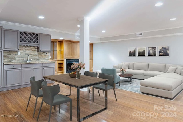 dining area with wine cooler, light hardwood / wood-style floors, crown molding, ornate columns, and sink