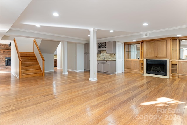 unfurnished living room with light hardwood / wood-style flooring, crown molding, brick wall, and decorative columns