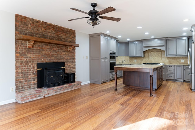 kitchen with a kitchen island, backsplash, gray cabinetry, a kitchen bar, and light wood-type flooring