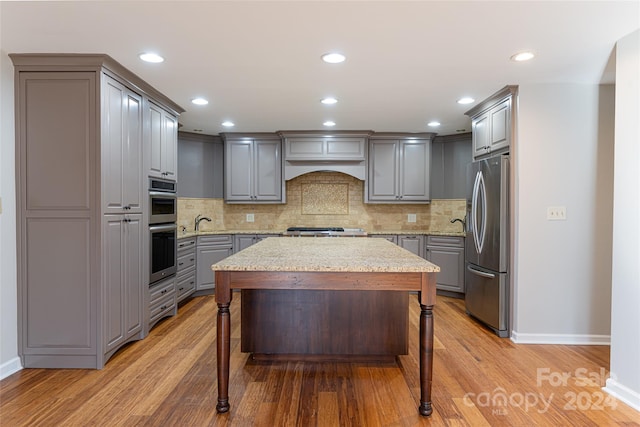 kitchen with light wood-type flooring, appliances with stainless steel finishes, light stone counters, tasteful backsplash, and a kitchen bar