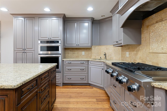 kitchen featuring stainless steel appliances, tasteful backsplash, custom exhaust hood, light wood-type flooring, and sink