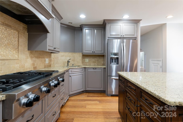 kitchen featuring light wood-type flooring, custom range hood, stainless steel appliances, sink, and tasteful backsplash