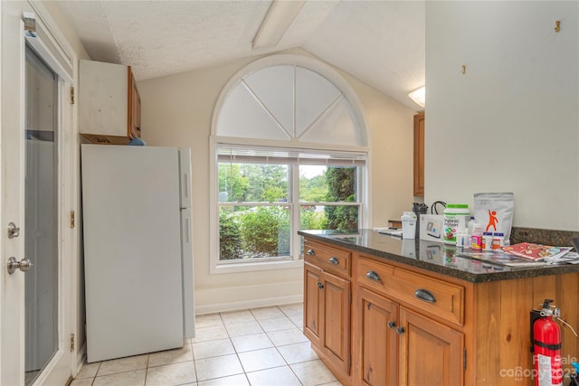 kitchen with dark stone counters, white refrigerator, light tile floors, a textured ceiling, and vaulted ceiling