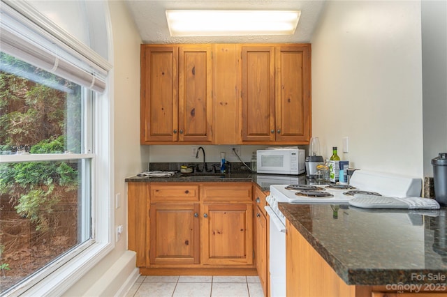 kitchen with white appliances, dark stone counters, sink, and light tile floors