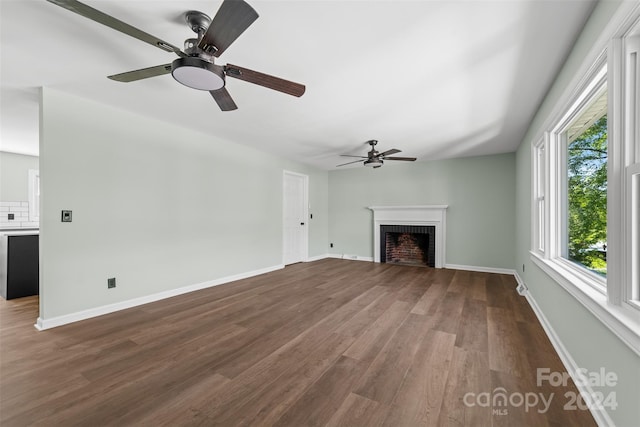 unfurnished living room with ceiling fan, a fireplace, dark hardwood / wood-style floors, and plenty of natural light