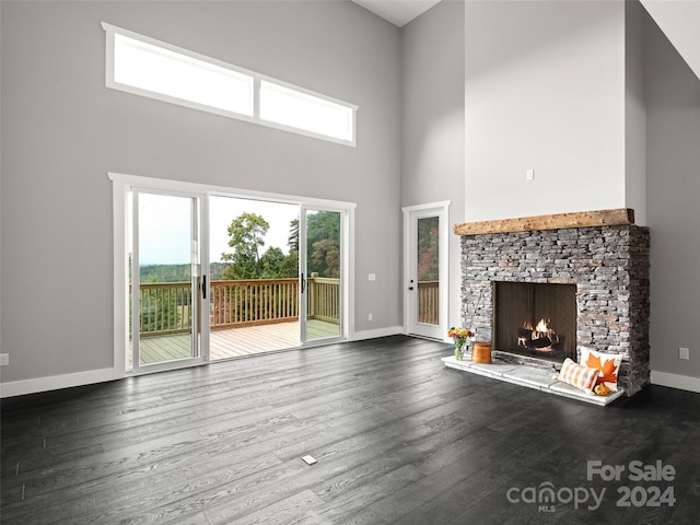 unfurnished living room featuring hardwood / wood-style flooring, a stone fireplace, and a towering ceiling