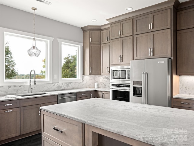 kitchen featuring light stone countertops, backsplash, stainless steel appliances, sink, and decorative light fixtures