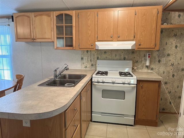 kitchen with light tile patterned floors, sink, kitchen peninsula, and white range with gas stovetop