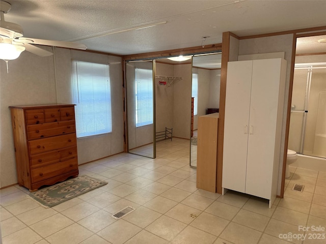 unfurnished bedroom with ensuite bath, a textured ceiling, light tile patterned floors, ceiling fan, and a closet