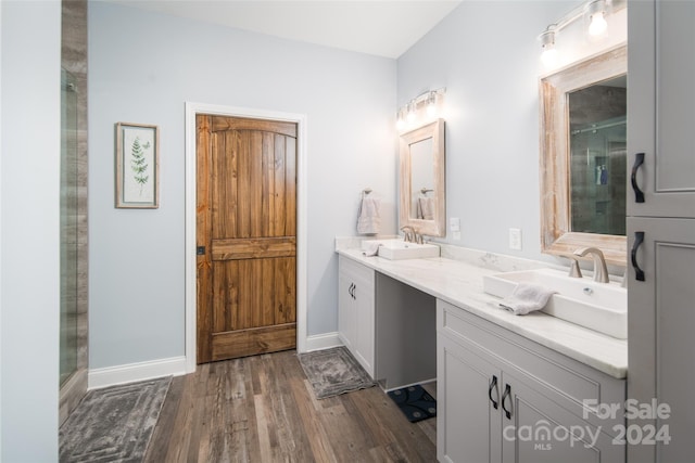 bathroom featuring dual bowl vanity, a shower with shower door, and wood-type flooring