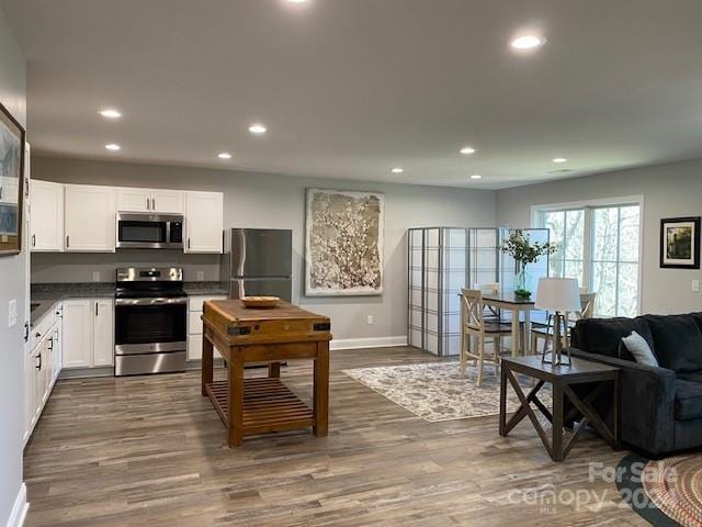 kitchen with dark hardwood / wood-style floors, stainless steel appliances, dark stone counters, and white cabinetry