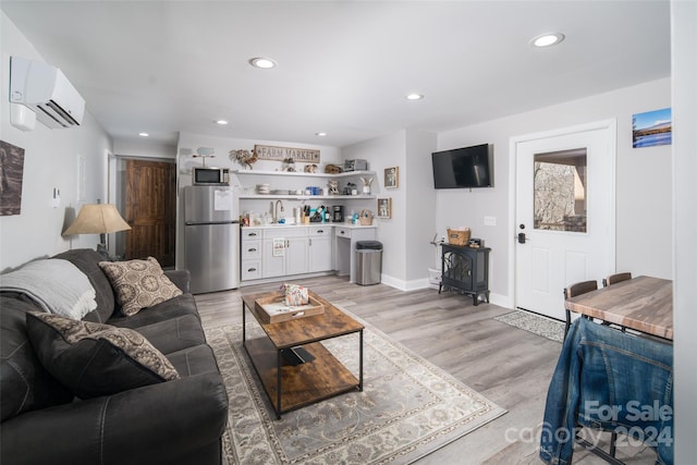 living room with a wall unit AC, a wood stove, light hardwood / wood-style flooring, and sink