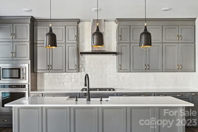 kitchen with wall chimney exhaust hood, a center island with sink, decorative light fixtures, and appliances with stainless steel finishes