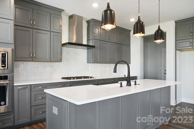 kitchen with dark hardwood / wood-style floors, an island with sink, stainless steel appliances, gray cabinets, and wall chimney exhaust hood