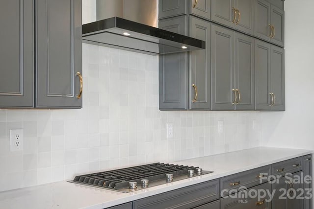 kitchen with backsplash, stainless steel gas stovetop, gray cabinets, and wall chimney range hood