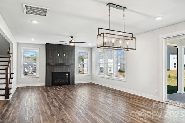 unfurnished living room featuring ceiling fan with notable chandelier, a large fireplace, and dark wood-type flooring