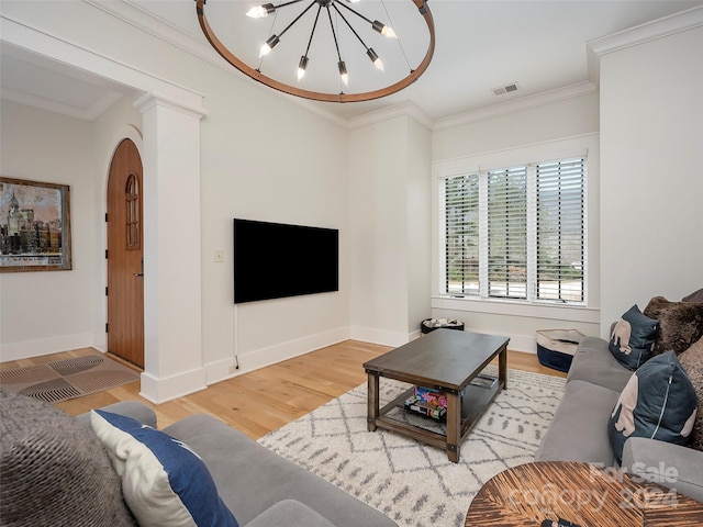 living room featuring an inviting chandelier, ornamental molding, decorative columns, and light wood-type flooring