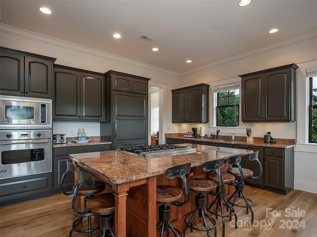 kitchen featuring light stone counters, a kitchen breakfast bar, appliances with stainless steel finishes, light hardwood / wood-style flooring, and a center island