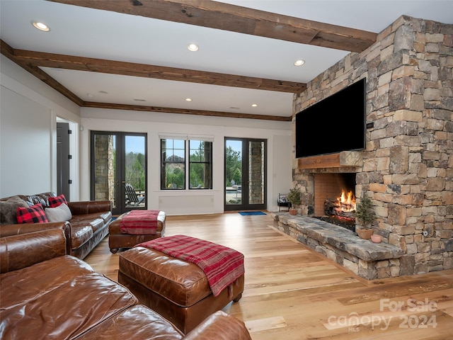 living room featuring beam ceiling, french doors, light hardwood / wood-style floors, and a stone fireplace