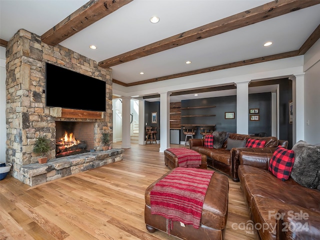 living room featuring beamed ceiling, a fireplace, light wood-type flooring, ornate columns, and ornamental molding