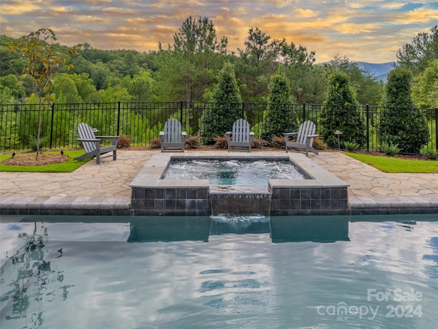 pool at dusk featuring an outdoor hot tub, a patio, and pool water feature