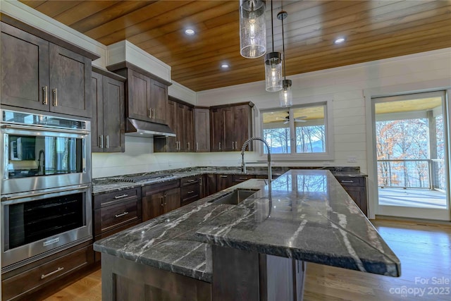 kitchen featuring a kitchen island with sink, hanging light fixtures, appliances with stainless steel finishes, light hardwood / wood-style flooring, and wooden ceiling