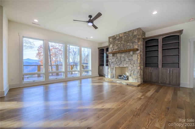 unfurnished living room featuring a fireplace, ceiling fan, dark wood-type flooring, and a wealth of natural light