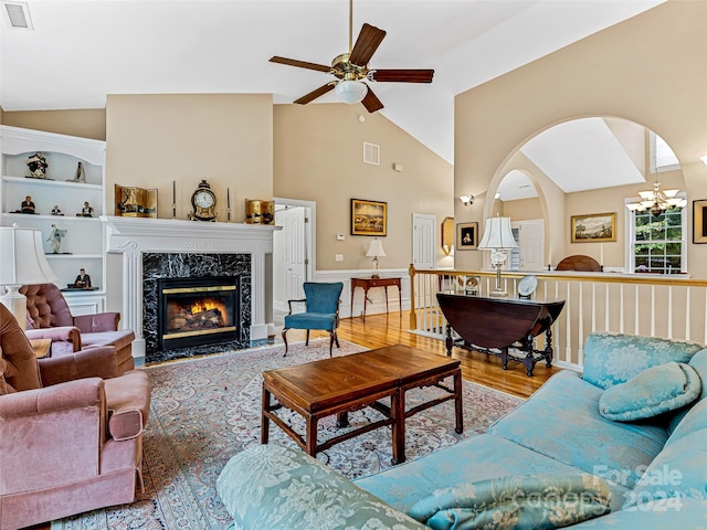 living room featuring lofted ceiling, ceiling fan with notable chandelier, hardwood / wood-style flooring, built in shelves, and a premium fireplace
