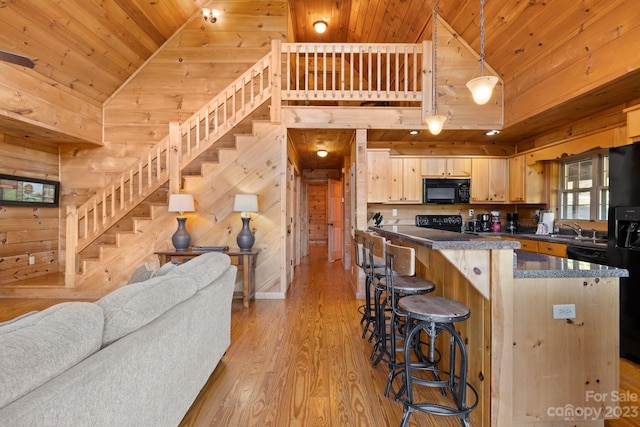 kitchen featuring black appliances, high vaulted ceiling, light brown cabinetry, wood ceiling, and a breakfast bar area