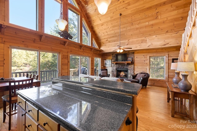 kitchen featuring ceiling fan, light hardwood / wood-style flooring, a fireplace, wood walls, and high vaulted ceiling