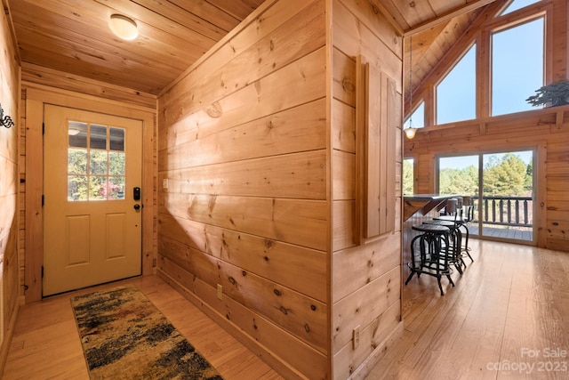 doorway to outside featuring wooden walls, wooden ceiling, lofted ceiling, and light hardwood / wood-style floors