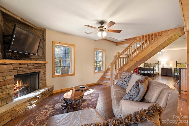 living room with ceiling fan, dark wood-type flooring, and a stone fireplace